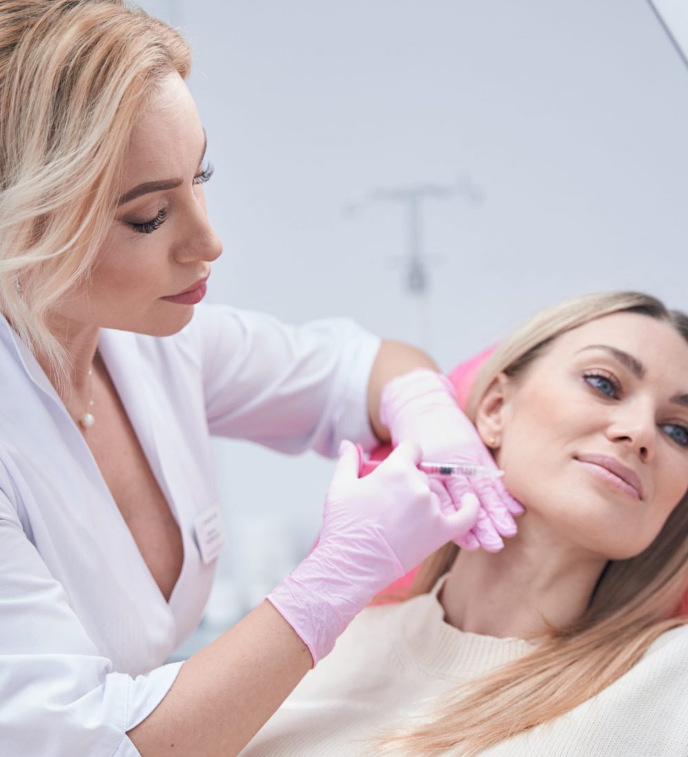 Focused aesthetic clinic doctor injecting dermal filler into cheek area of patient