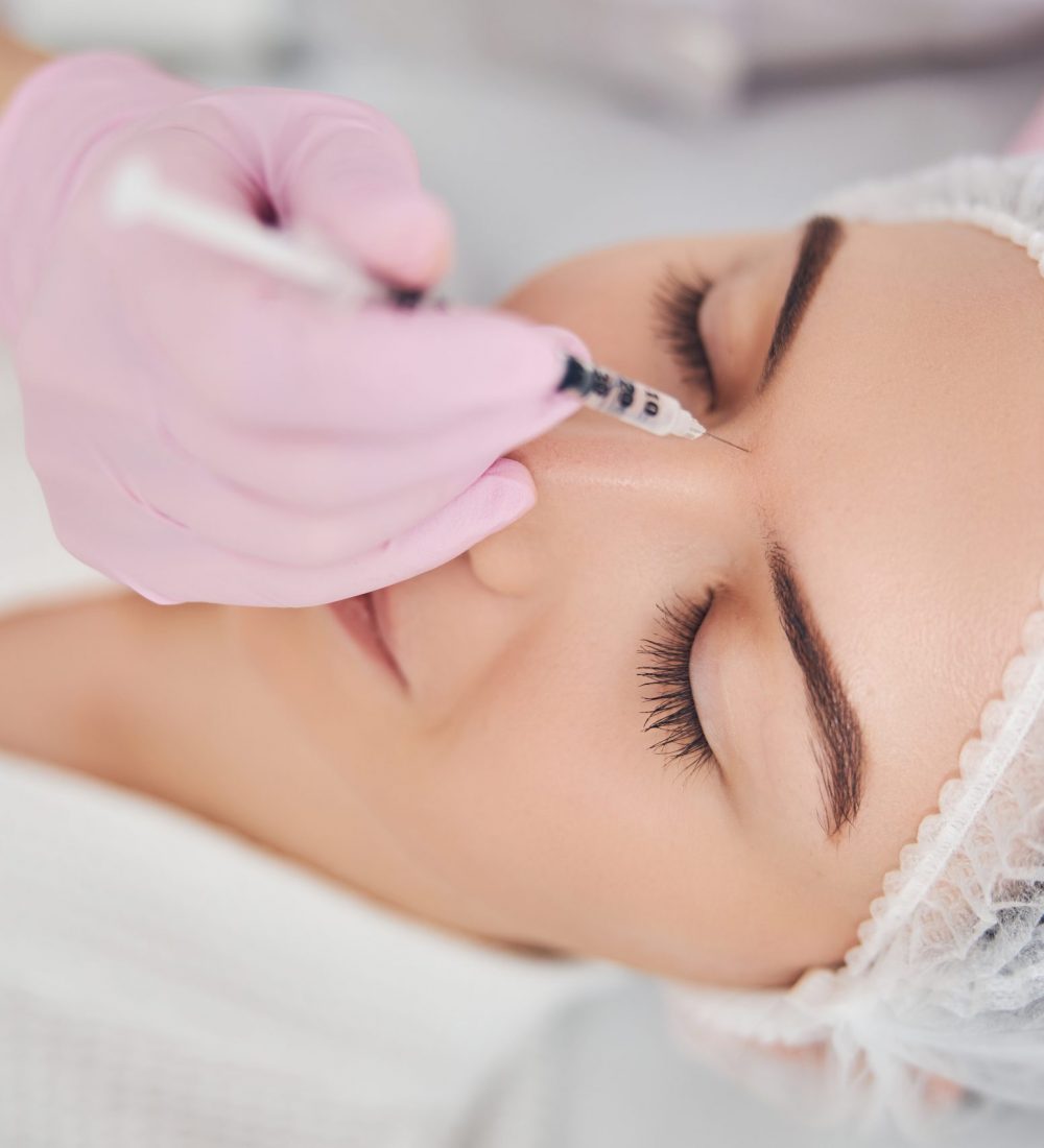 Beautician hand introducing a syringe between woman eyebrows for face skin enhancement